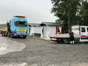Lastbil, servicebil och person i varselkläder vid två hus täckt med vit plast på Björkstaholmen.
