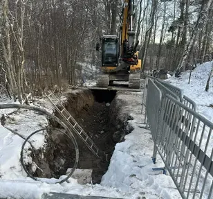 Grävd ränna med nedlagda ledningar, omgiven av jordhögar och grävmaskin i bakgrunden.