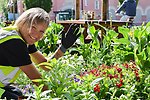 Person planterar blommor och hälsar mot kameran.